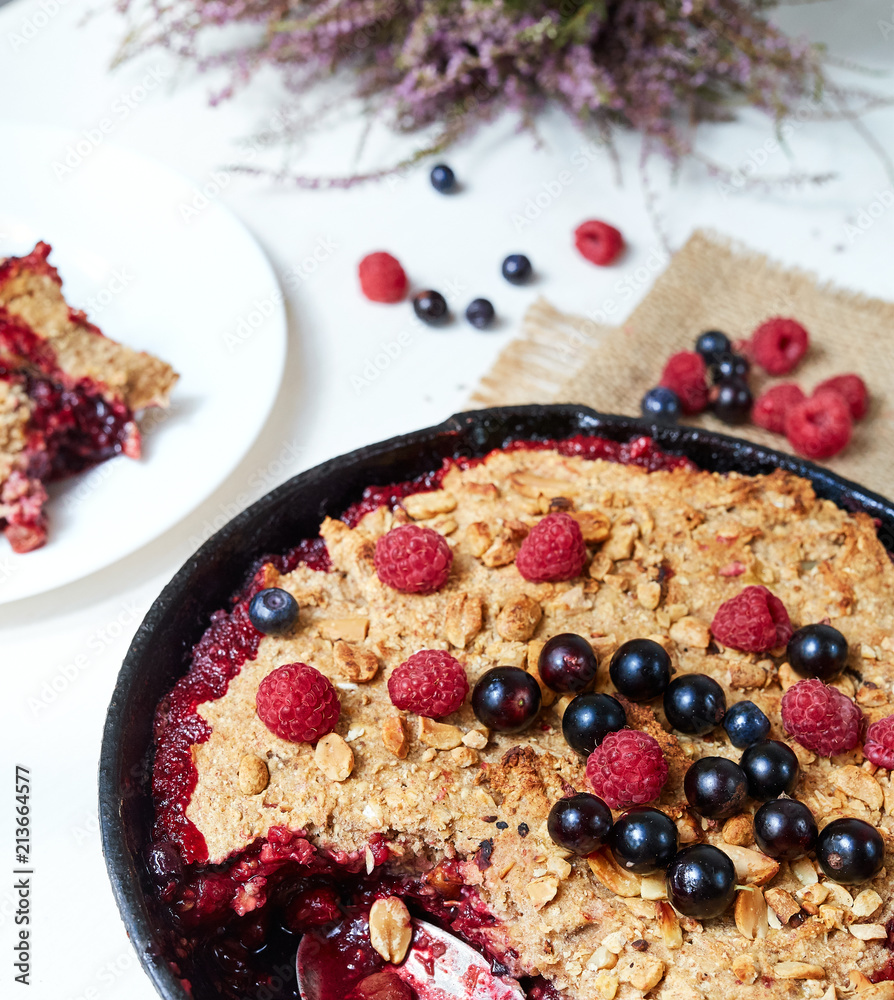 Berry crumble in the black cast-iron frying pan on the white table Berry crumble in the black cast-iron frying pan on the white table