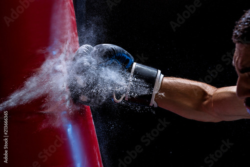 Close-up hand of boxer at the moment of impact on punching bag over black background
