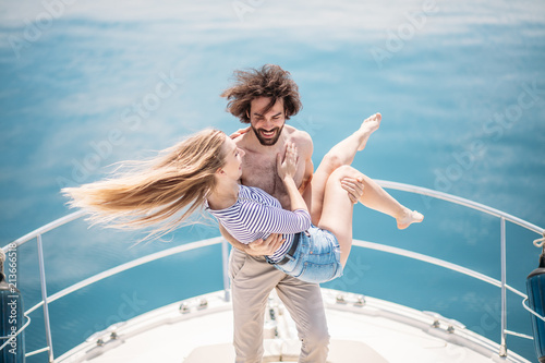 Hot young lovers starting foreplay on the bow of the luxury boat in open sea in summer. Young brunette man holding on hands sensual blonde woman. Outdoor portrait of sea travel recreation lifestyle.
