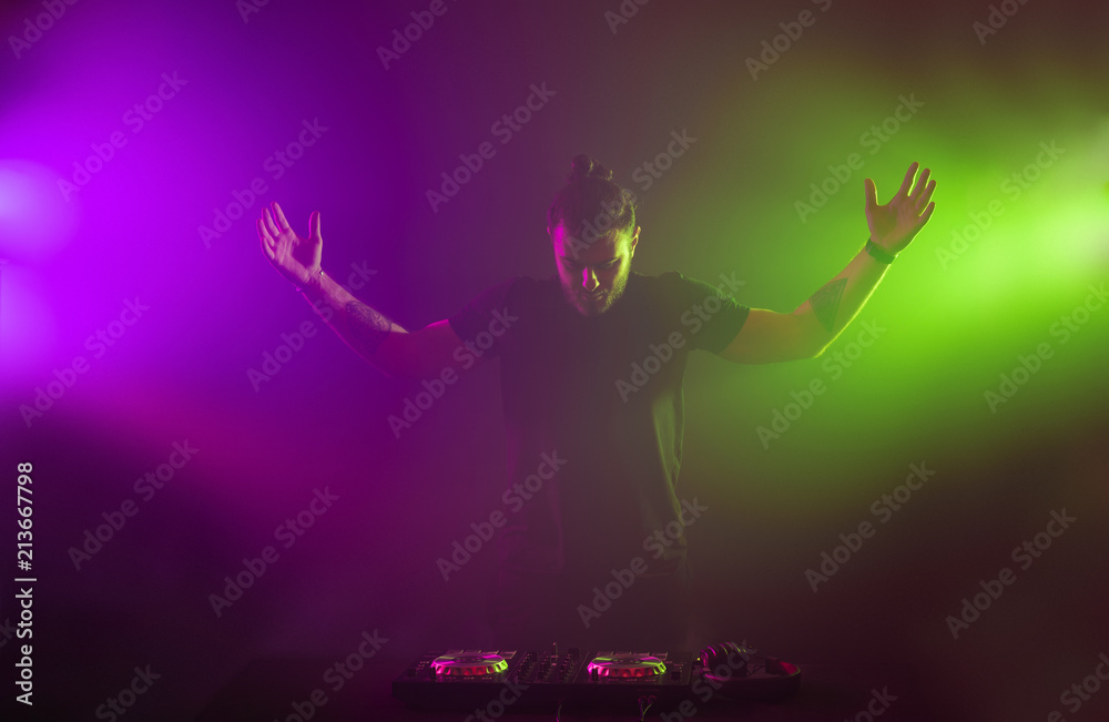 DJ at work mixing sound on her decks at a party or night club with colourful smoke light background