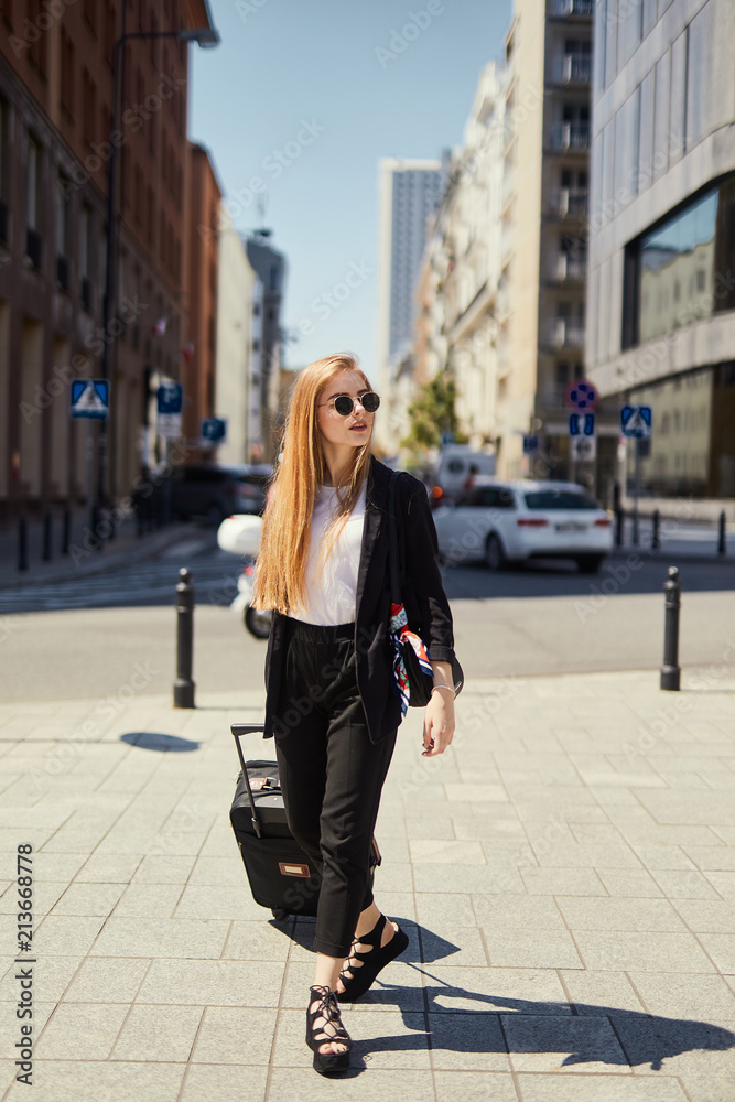 Blonde girl walking on the street with suitcase