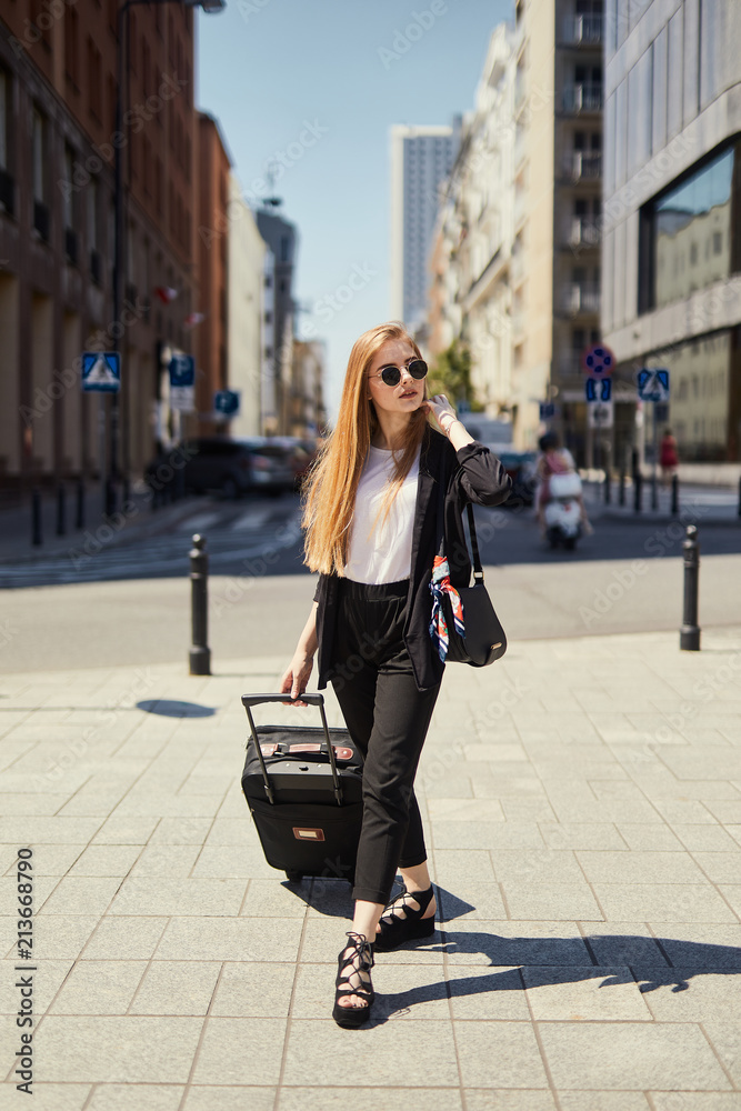 Fototapeta premium Blonde girl walking on the street with suitcase