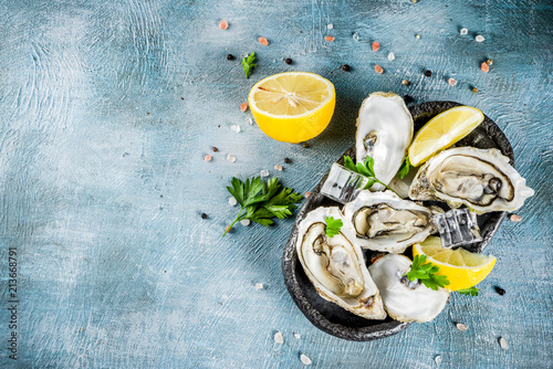Fotografia Fresh raw seafood, oysters with lemon and ice on a light blue background