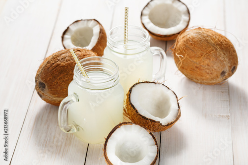 Refreshing coconut water in jars and coconuts on a wooden white background.