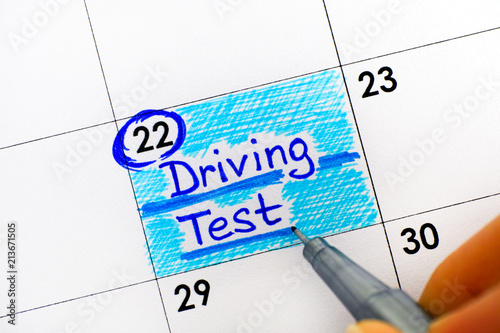 Woman fingers with pen writing reminder Driving Test in calendar. photo