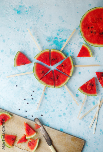 Fresh organic watermelon slice popsicles on light blue background. Top view, selective focus. Tasty summer fruit, healthy lifestyle