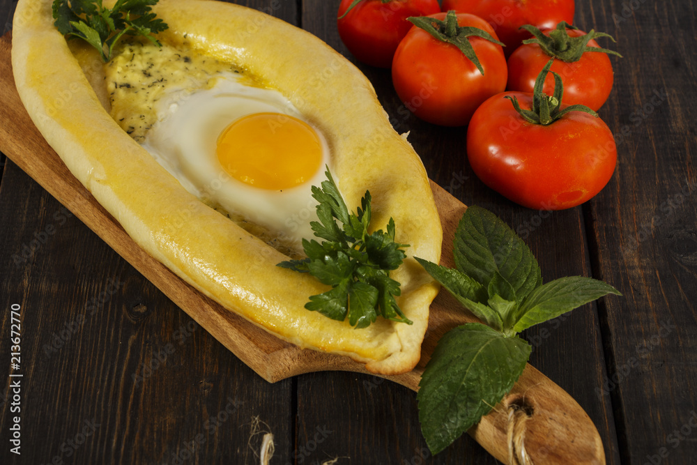 Khachapuri with fresh vegetables caucasian kitchen, close-up on a black wooden table. Adzharian khachapuri. View from above Khachapuri with fresh vegetables caucasian kitchen, close-up on a black wooden table. Adzharian khachapuri. View from above