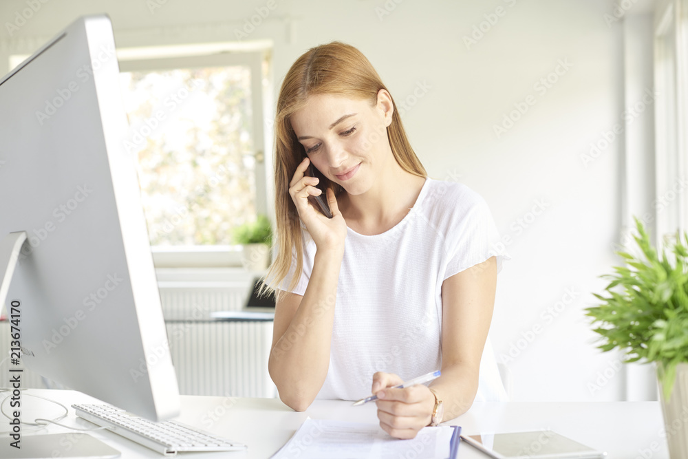Young professional woman making a call on her mobile phone while working on computer. Home office Young professional woman making a call on her mobile phone while working on computer. Home office