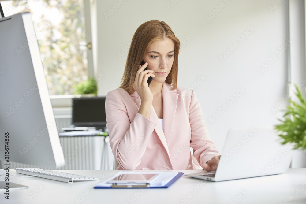 Young professional woman making a call on her mobile phone while working on computer. Home office Young professional woman making a call on her mobile phone while working on computer. Home office