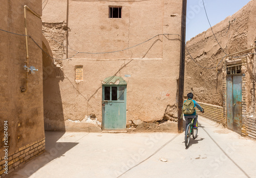Fototapeta Naklejka Na Ścianę i Meble -  YAZD, IRAN - MAY 2, 2017. A small boy riding his bike on the streets of Yazd old town. Authentic and beautiful photo, warm Persian and Arabic style and atmosphere
