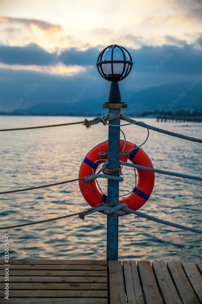 Fototapeta premium pier with lamp and lifebuoy at sunset