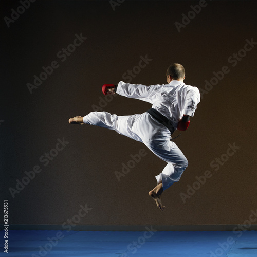 A man in karategi trains a kicking in a jump