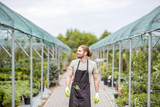Handsome worker in uniform walking at the greenhouse with green plants for sale