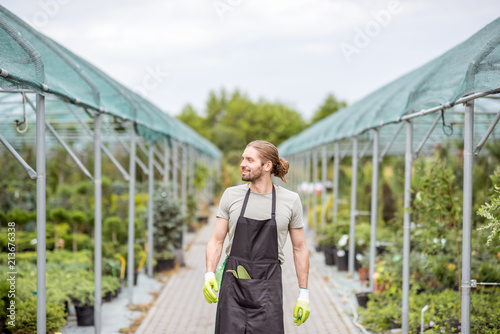 Handsome worker in uniform walking at the greenhouse with green plants for sale © rh2010
