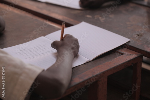 african education - close up of a school kid sitting inside a classroom, holding a pencil, indoors on a sunny day