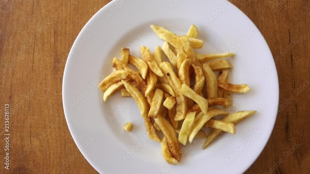 A plate of fried potatoes rotates against the background of a wooden table. Potato - chips, as a side dish for a meat dish for lunch. A plate of fried potatoes rotates against the background of a wooden table. Potato - chips, as a side dish for a meat dish for lunch.