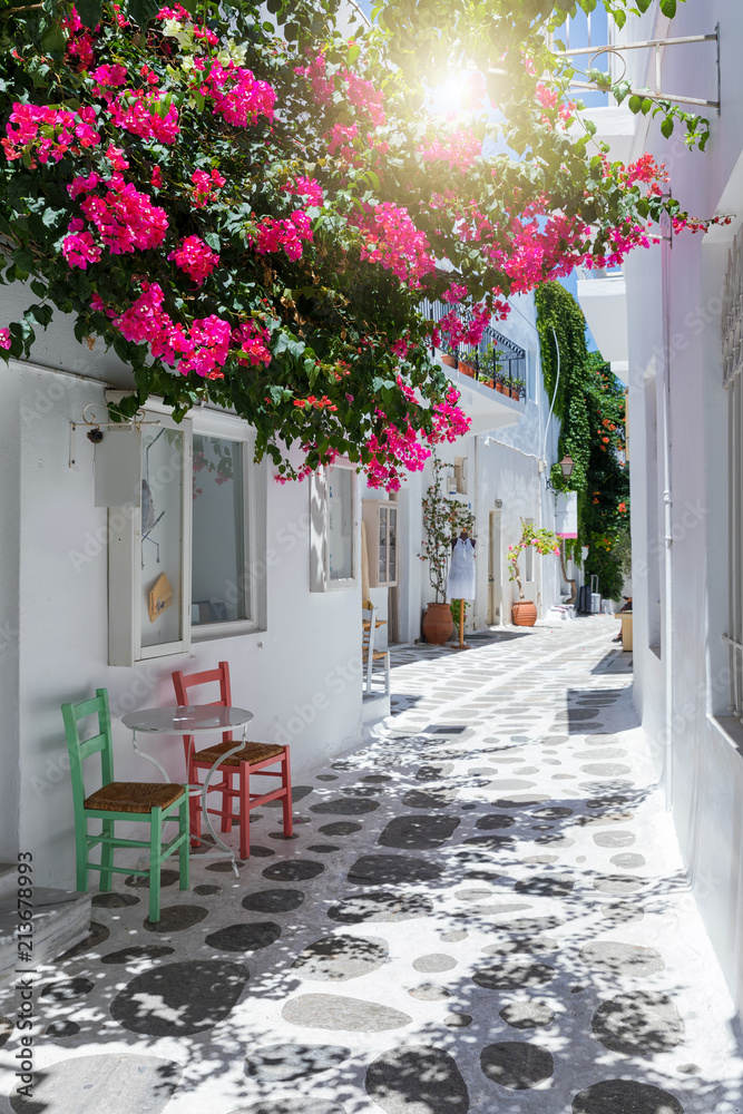 Fototapeta premium Aleja z kolorowymi kwiatami bugenwilli, białymi domami i kolorowymi krzesłami w Parikia, Paros, Cyklady, Grecja