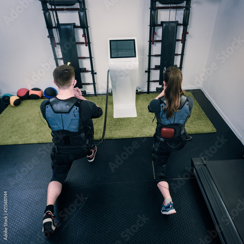 Back view of man and woman in electro muscular stimulation suits squatting photo