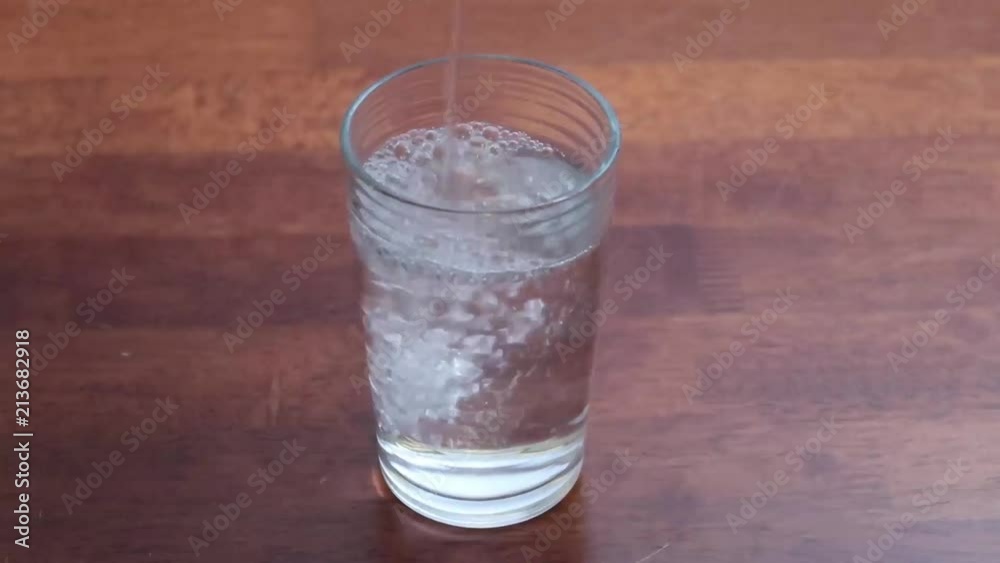 Pouring water into a glass and popping in two asprin tablets Pouring water into a glass and popping in two asprin tablets