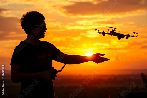 silhouette of a man launches a drone with a remote in the sunset light © yurakrasil