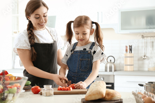 Young nanny with cute little girl cooking together in kitchen