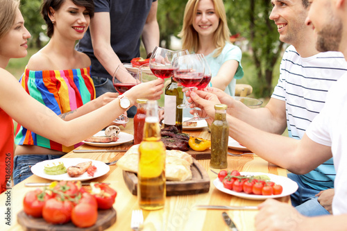 Young people with glasses of wine at table outdoors. Summer barbecue