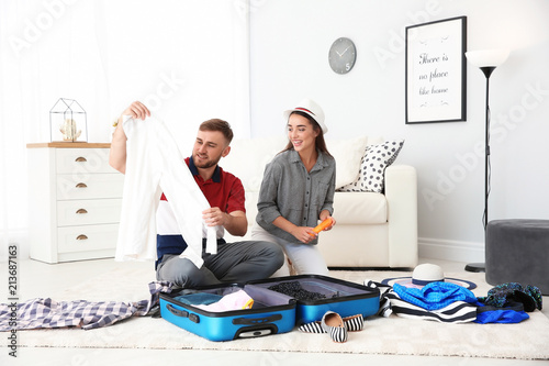 Young couple packing suitcase for summer journey at home