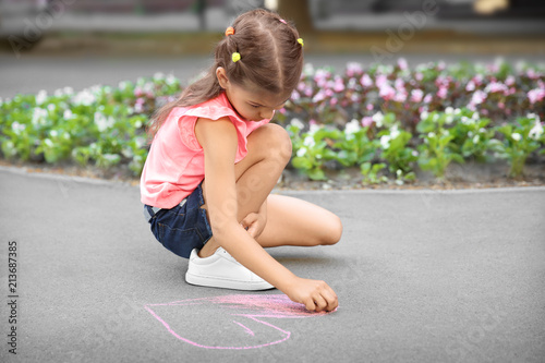 Little child drawing heart with chalk on asphalt