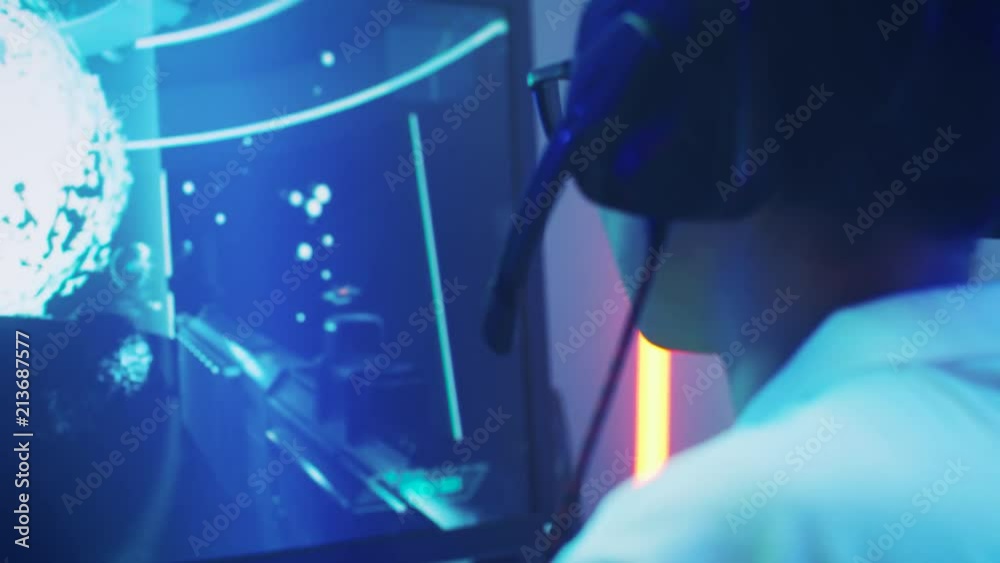 Professional Gamer Playing in First-Person Shooter Online Video Game on His Personal Computer. He's Talking with His Team Through Headset. Professional Gamer Playing in First-Person Shooter Online Video Game on His Personal Computer. He's Talking with His Team Through Headset.