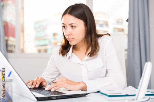 Girl working  with laptop and documents at table in office
