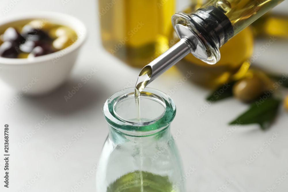 Pouring fresh olive oil into bottle on table Pouring fresh olive oil into bottle on table