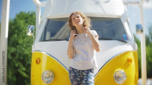 young woman outdoors by yellow vagon car listening music in headphones using smartphone - relaxing, enjoying, concept of technology and travel photo