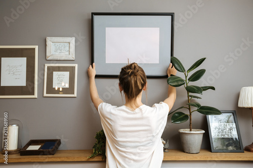 Girl hanging a frame on a gray wall photo