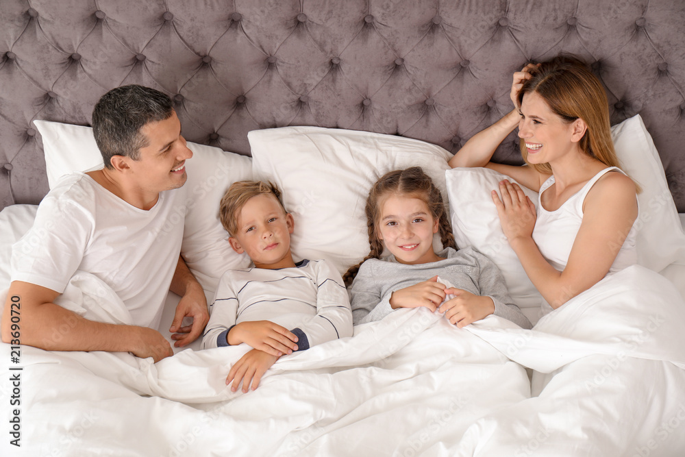 Couple with children lying under blanket in bed. Happy family