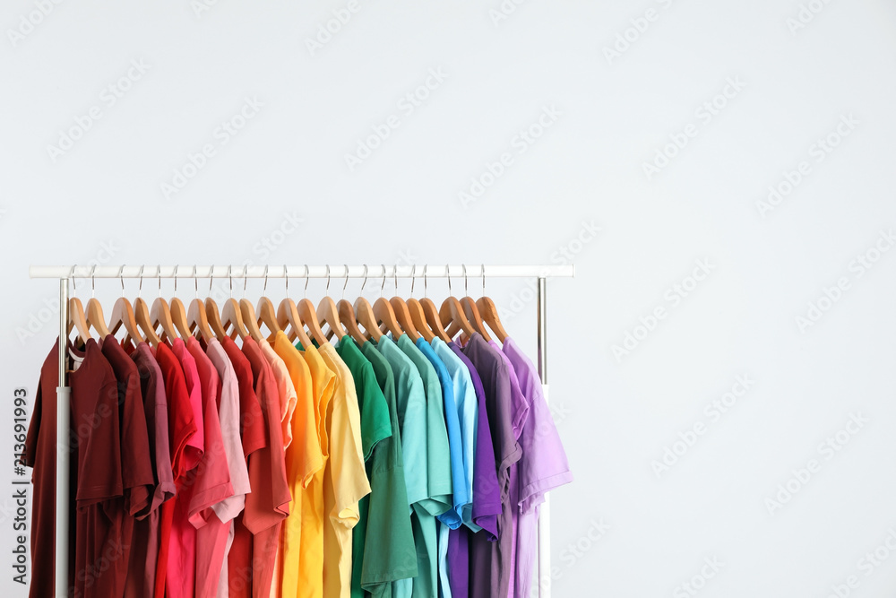 Rack with rainbow clothes on light background