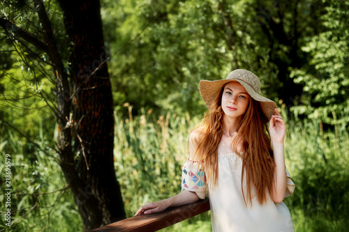 A sophisticated red-haired girl in a simple linen dress, in a light wide-brimmed hat. Model look. Natural beauty. Artistic portrait