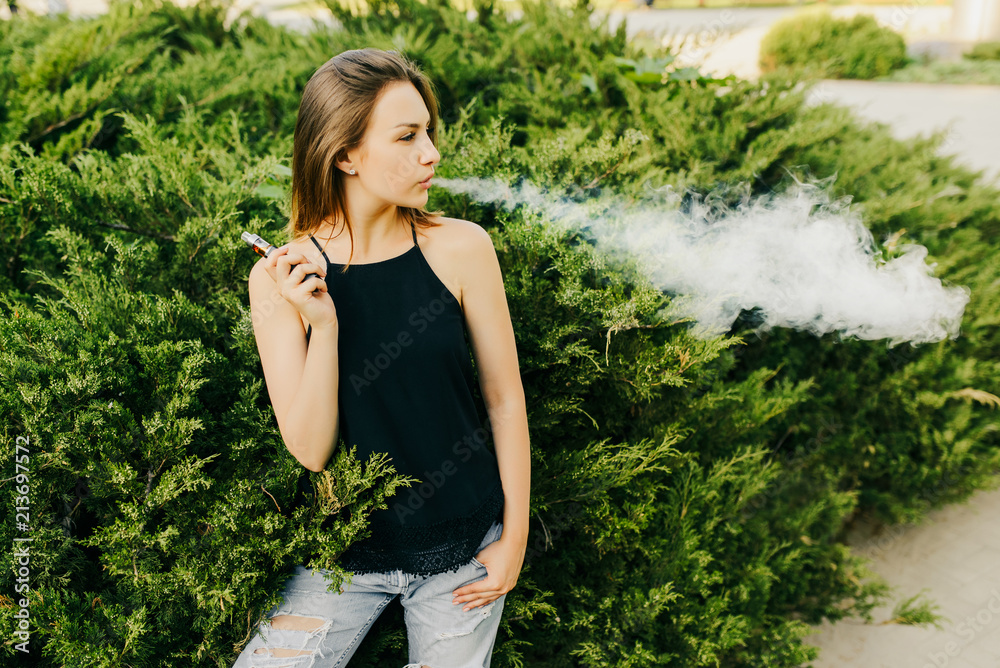 Fashionable girl smoking an e-cigarette outside