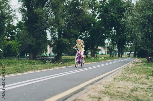 little child riding bicycle on road in park on summer day