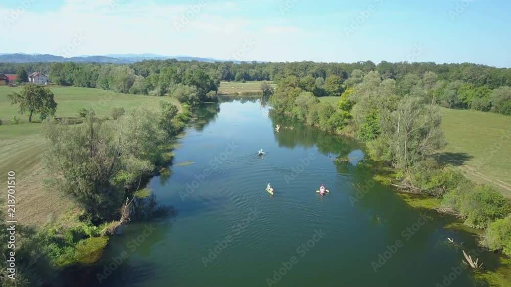 AERIAL: Flying behind a group of active tourists canoeing down a calm river running through the sunny green countryside in Slovenia. Young travelers on canoe trip paddling down a deep blue stream. AERIAL: Flying behind a group of active tourists canoeing down a calm river running through the sunny green countryside in Slovenia. Young travelers on canoe trip paddling down a deep blue stream.