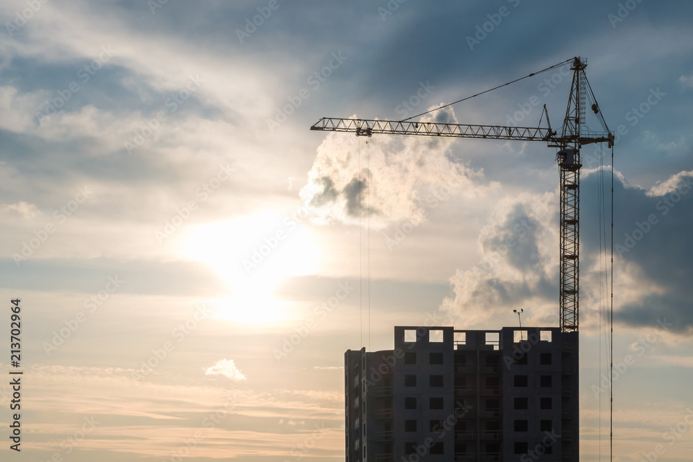 Tower cranes and unfinished multi-storey high near buildings under construction site in the evening