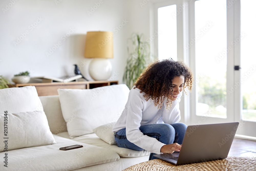 Smiling woman using laptop computer while sitting on sofa at home Smiling woman using laptop computer while sitting on sofa at home