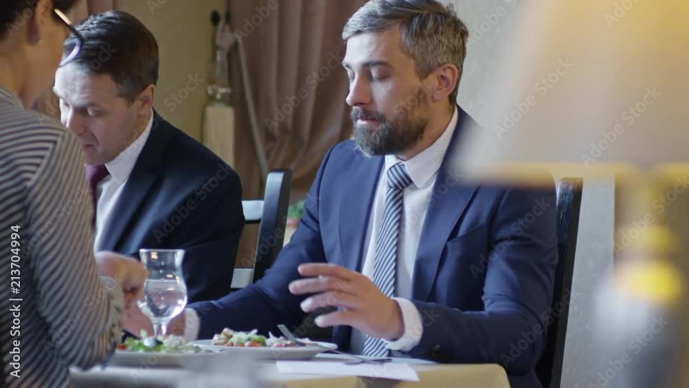 Group of three businesspeople enjoying tasty food at lunch together in restaurant or cafe and discussing work details Group of three businesspeople enjoying tasty food at lunch together in restaurant or cafe and discussing work details