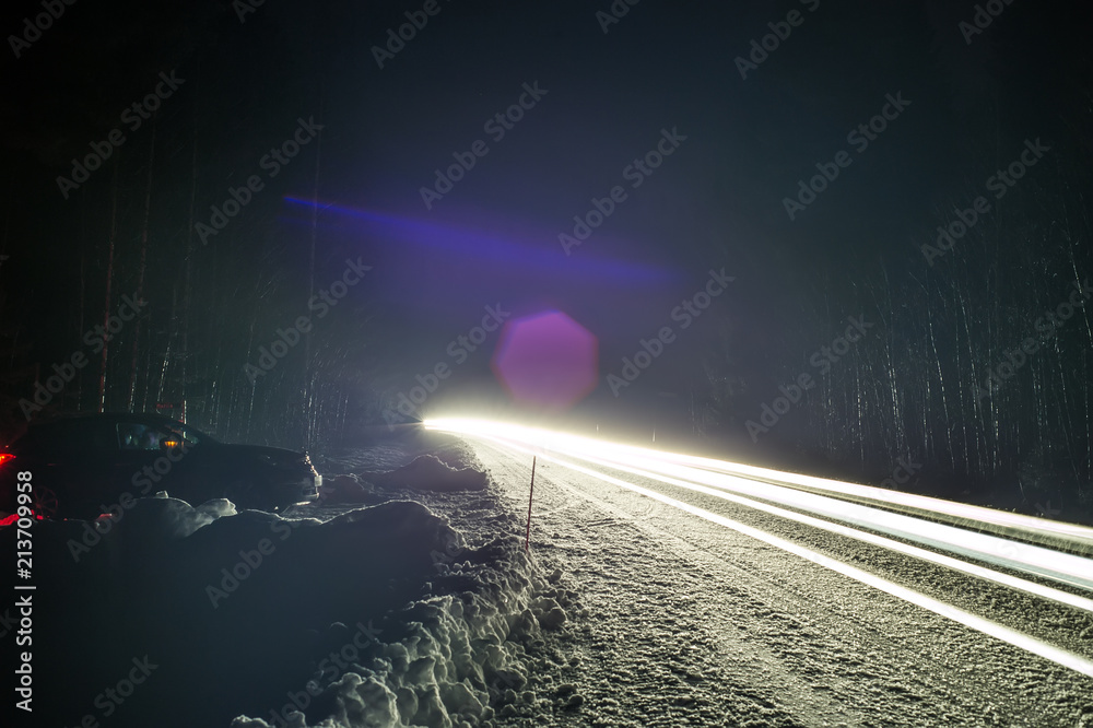 Car headlights on a winter road in the forest, on long exposure