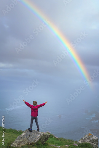 Girl on the top of a rock looking at rainbow