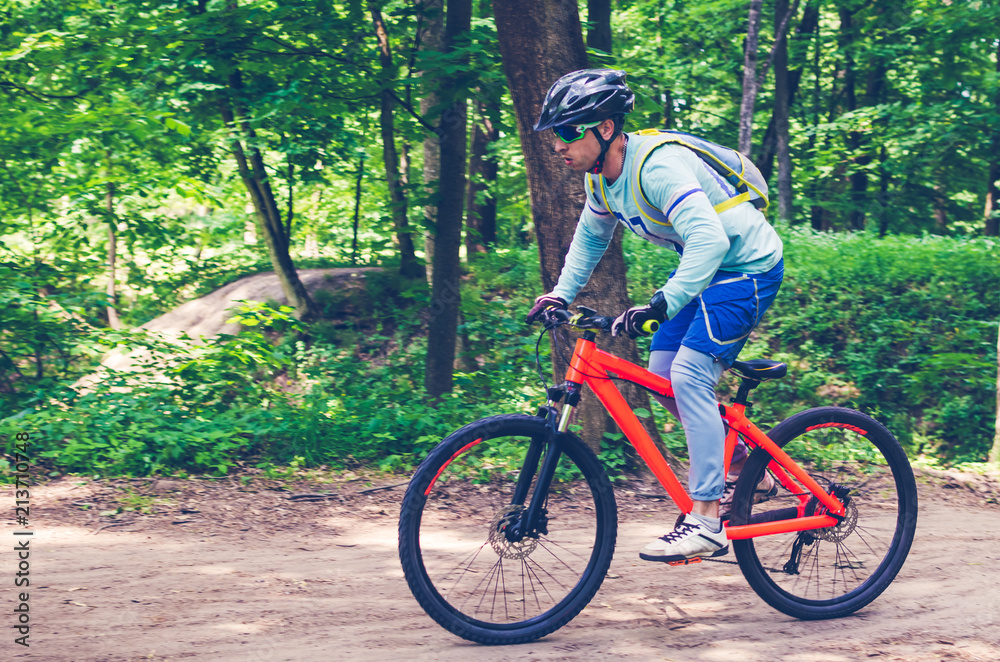 Cyclist in helmet on an orange bike doing a trick in a springboard jump in the forest, motion blur
