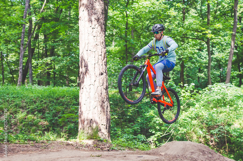 Cyclist in helmet on an orange bike doing a trick in a springboard jump in the forest, motion blur