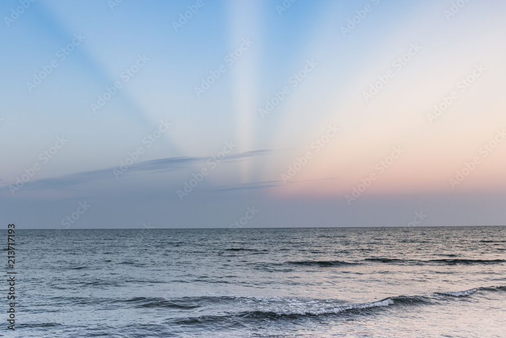 Rayos solares de colores entre nubes en el horizonte de un mar en calma y una pequeña ola.