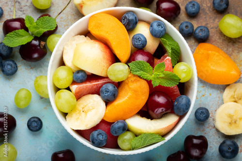 Bowl of healthy fresh fruit salad on a blue rusty background. Top view