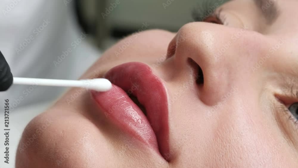Healthy spa. Young beautiful woman after permanent make-up tattoo on her lips. Applying red permanent make up tattoo on young girl lips. Close-up. Plastic medicine and cosmetology.