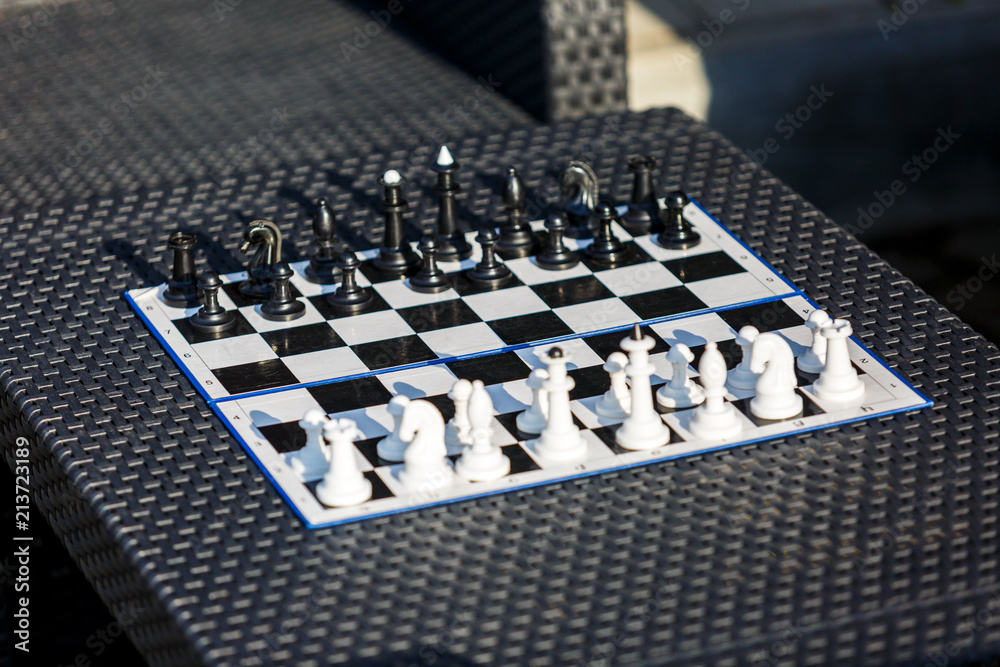 chessboard on the rattan table in the garden in the summer. Travel, vacation, holidays concept Education concept, chess lesson, training, intellectual game chessboard on the rattan table in the garden in the summer. Travel, vacation, holidays concept Education concept, chess lesson, training, intellectual game